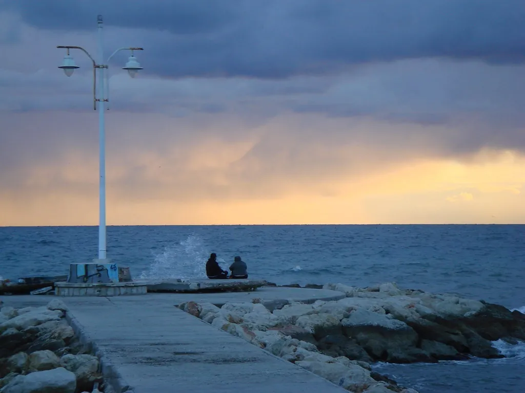 Espigón de Pedregalejo al atardecer, con una farola y dos personas mirando el mar