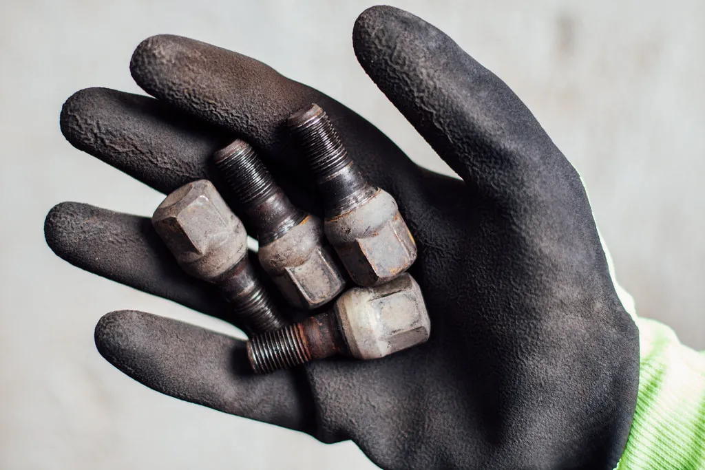 Mano con guante de trabajo sujetando varias tuercas de rueda